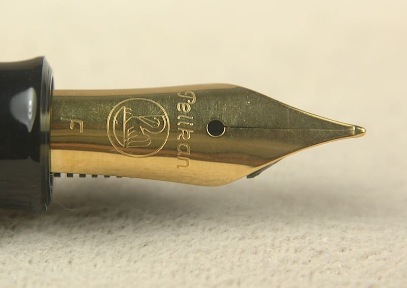 Gold fountain pen nib on textured surface.