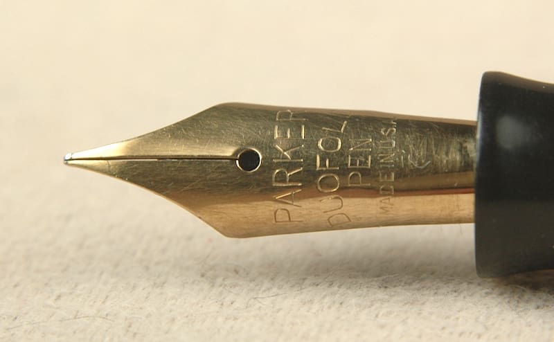 Gold fountain pen nib on paper background.