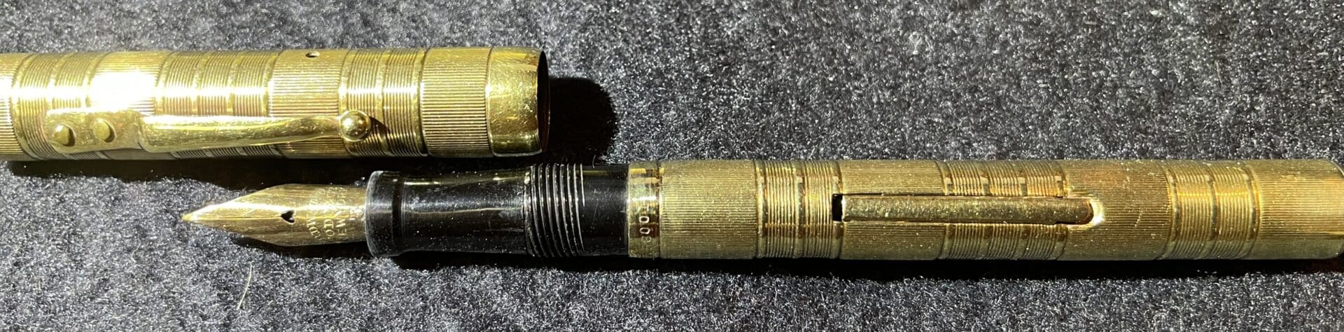 Vintage brass fountain pen on dark fabric.