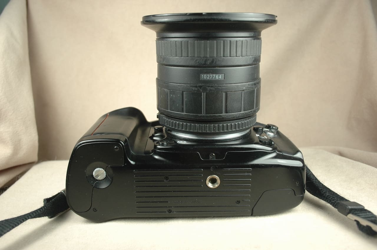Black DSLR camera with a zoom lens mounted, shown from the bottom view.