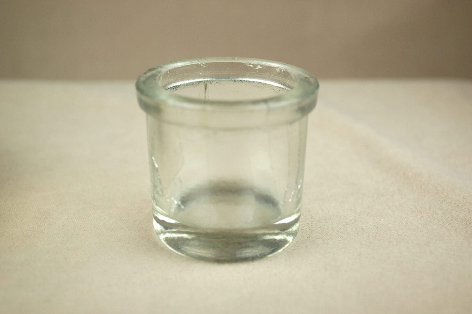 A clear glass container with a wide opening on a plain surface.