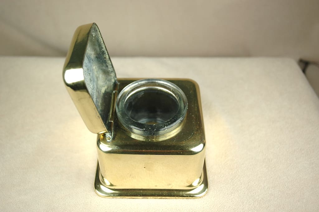 Vintage brass inkwell with hinged lid open, showing glass reservoir.