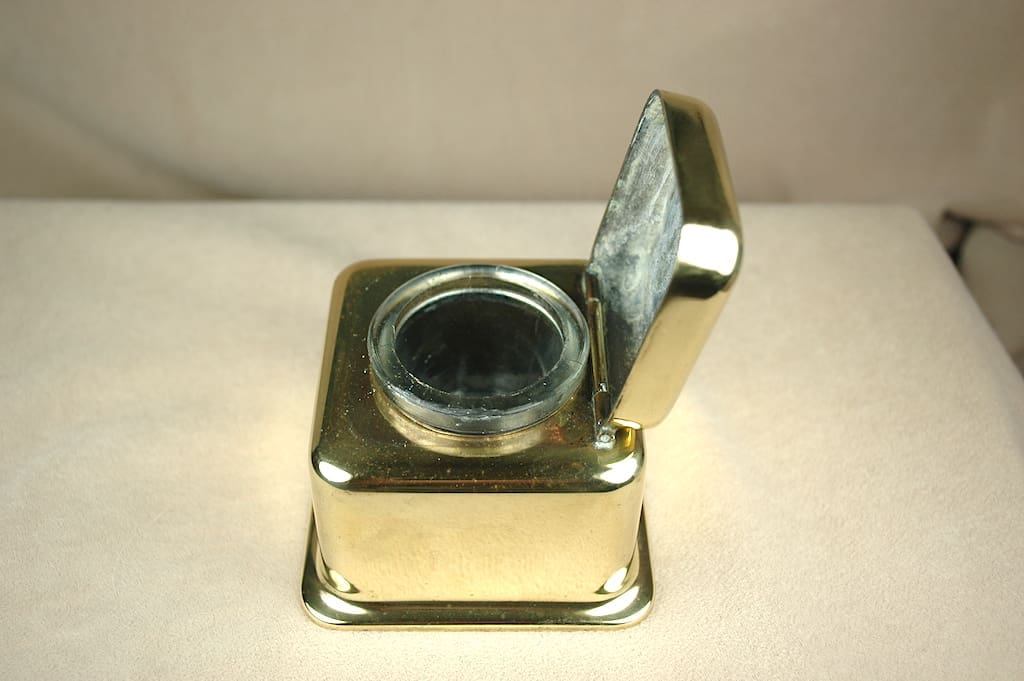 A vintage brass inkwell with a hinged lid open.