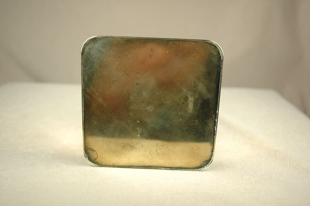 A small, square, tarnished metal box with rounded edges.