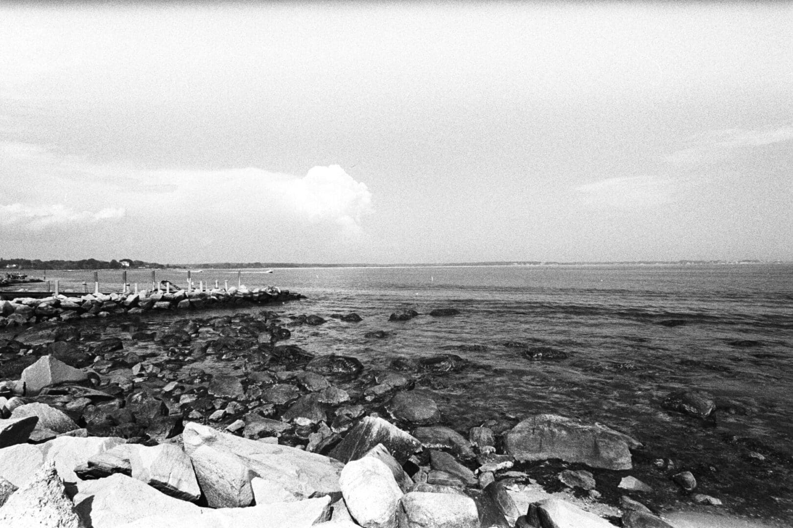 Black and white photo of a rocky shoreline with calm waters.