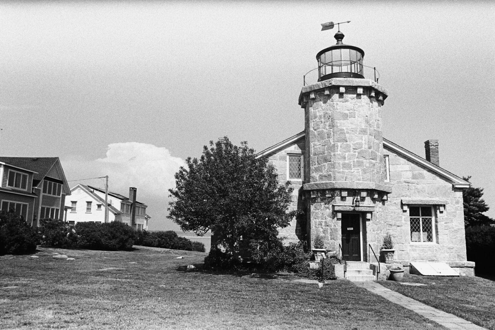 Historic stone lighthouse with adjacent buildings and a tree.