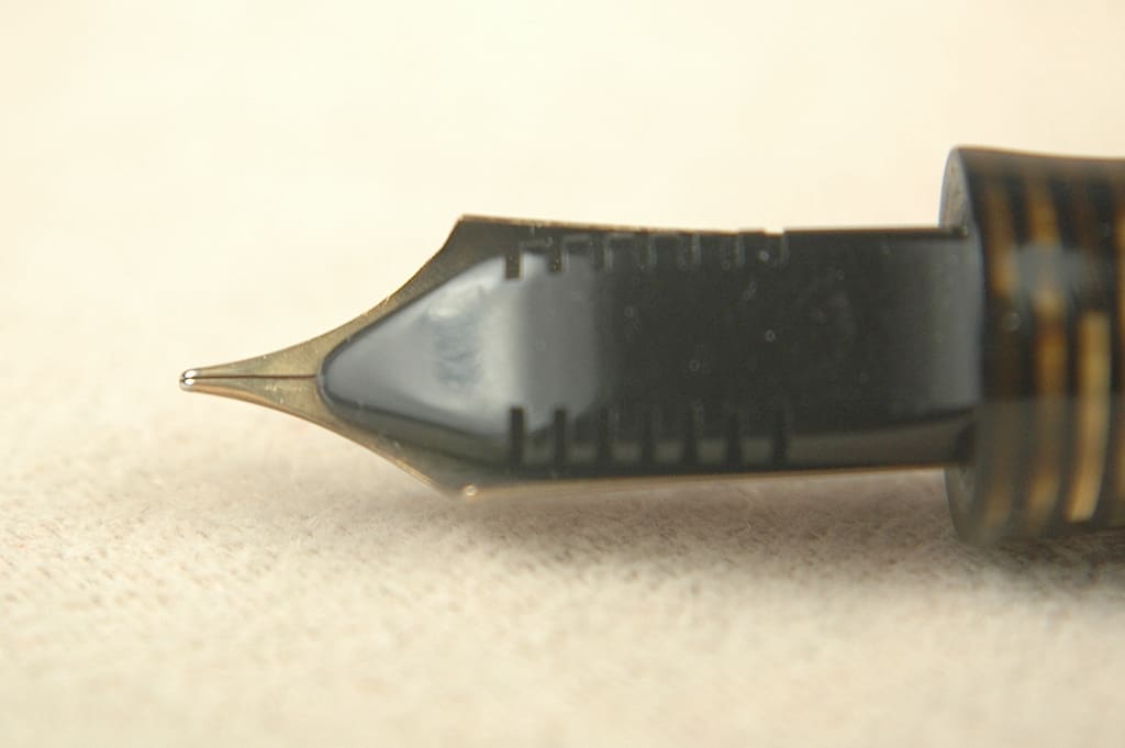 Close-up of a vintage fountain pen nib on a light surface.