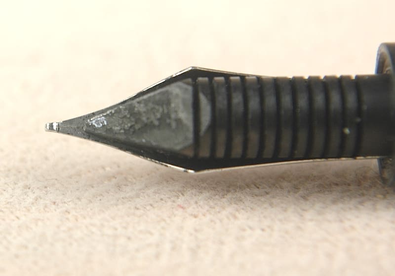 Close-up of a sharp, black fountain pen nib on a light surface.