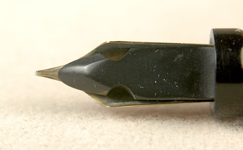 Close-up of a black fountain pen nib on a beige surface.