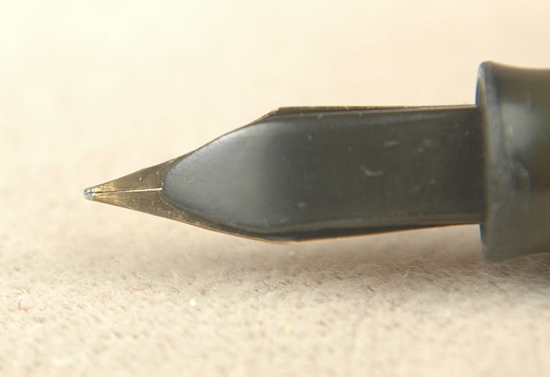 Close-up of a fountain pen nib on a beige surface.