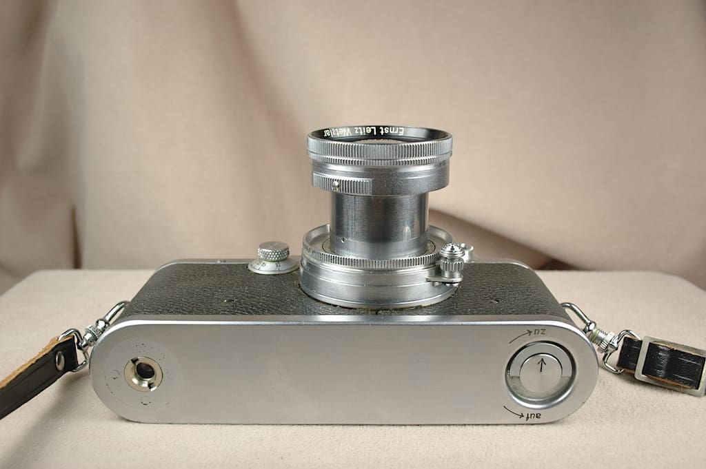 Vintage silver camera with an extended lens on a beige background.