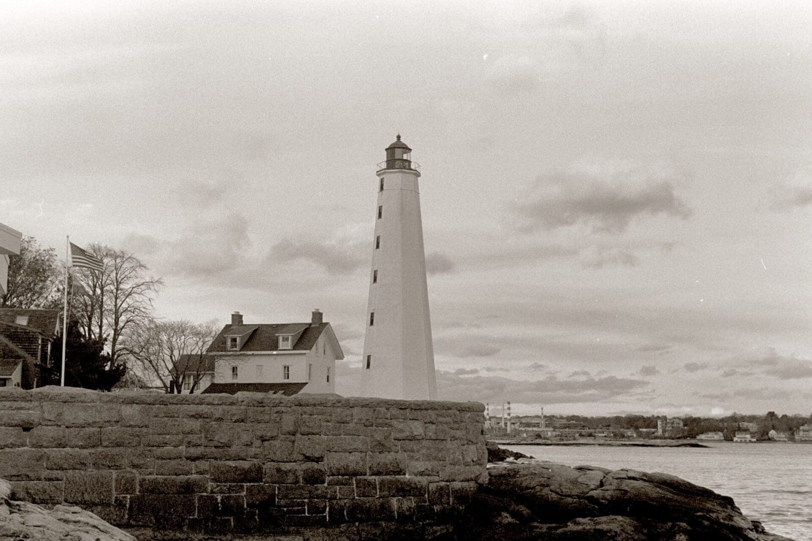 A tall lighthouse by the rocky shore under a cloudy sky.