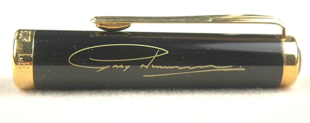 Close-up of a pen with a gold clip and signature on the barrel.