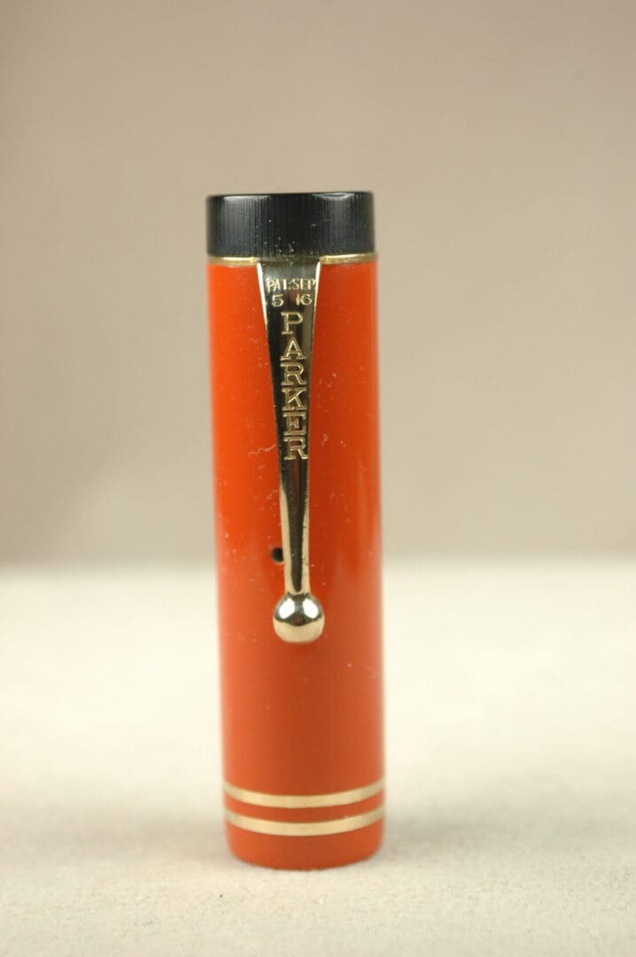 Close-up of a vintage orange lipstick tube with a silver clasp.