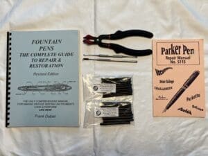 Tools and manuals for fountain pen repair and maintenance laid out on a white surface.